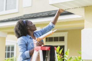 Woman on ladder outside house doing repairs