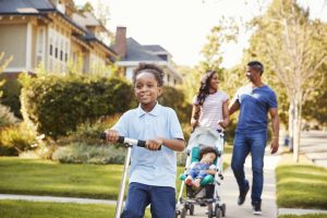 Couple Push Daughter In Stroller As Son Rides Scooter