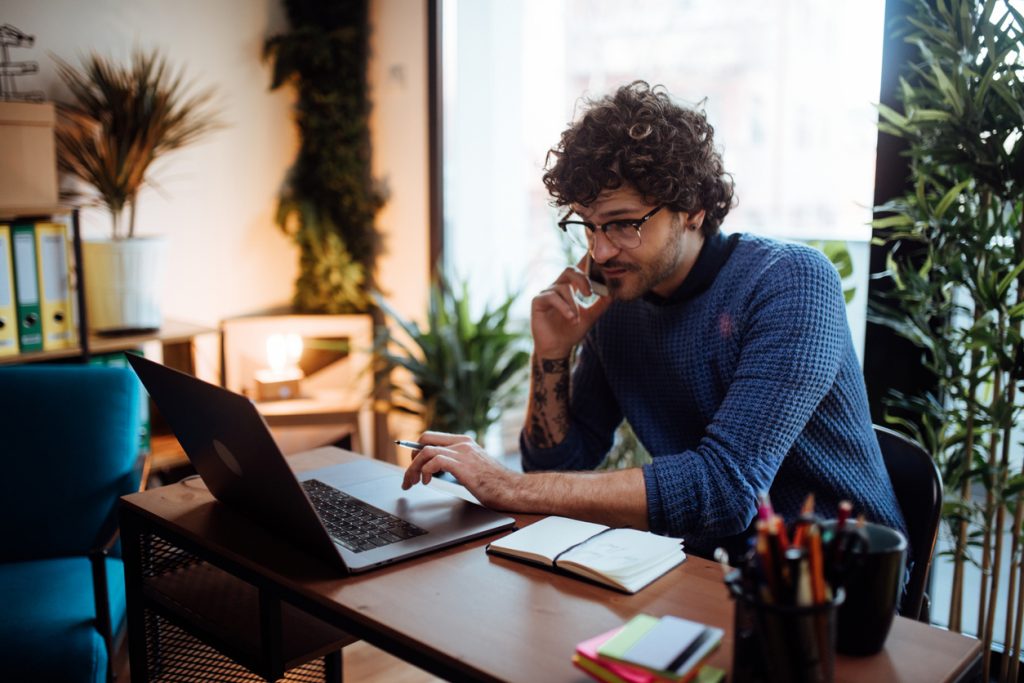 busy man working on his laptop while taking a call on his phone